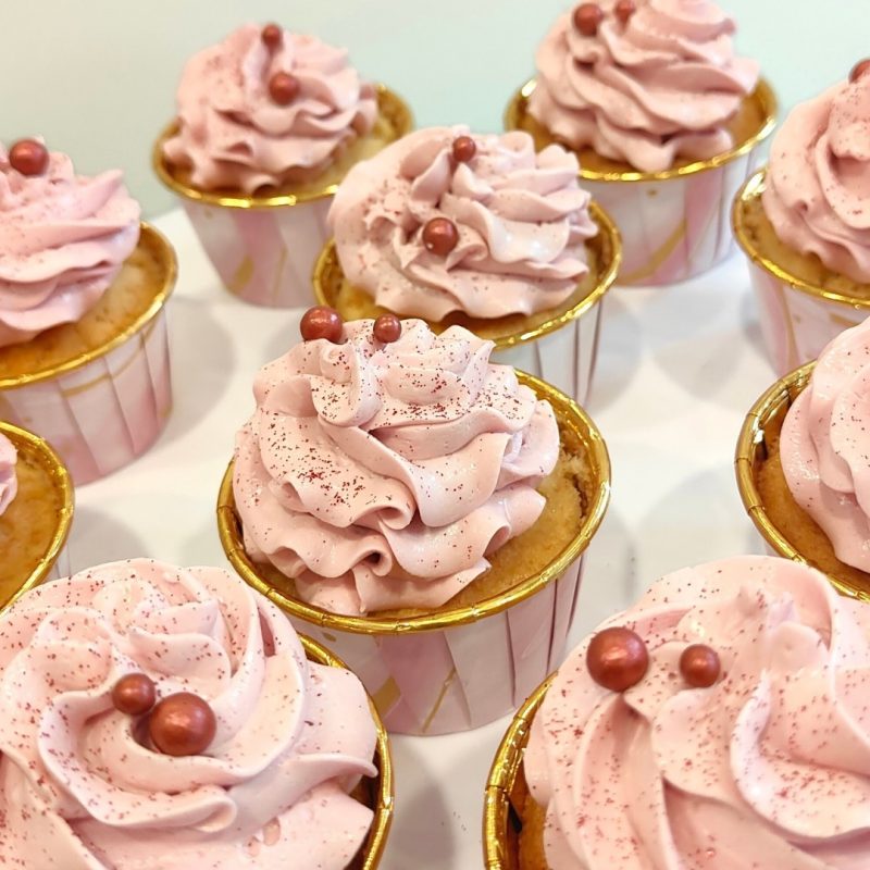 Cupcakes decorados con crema rosa y perlitas, ideales para complementar tartas personalizadas en Sevilla.